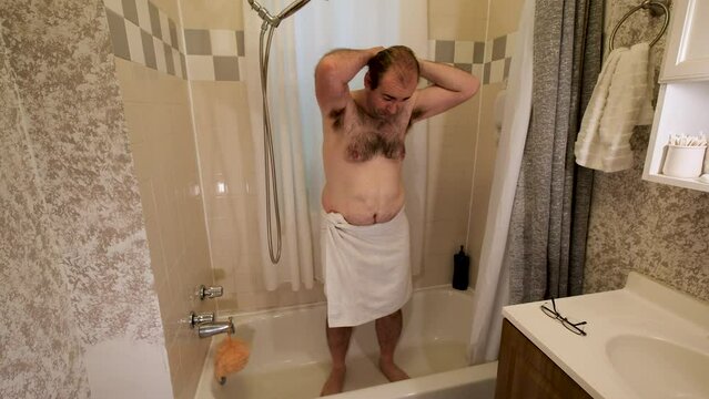Young male with just wrapped white towel around his waist getting into bathtub and preparing to get soak before washing.