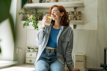 Happy young woman drinking water in kitchen at home