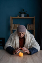 Tired senior man warms hands over candlelight at home no heating. Shutdown of heating and...