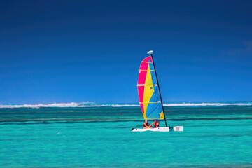 People on a color catamaran sailboat or winsurf sailing in calm caribbean sea, summer vacation and sport - Powered by Adobe