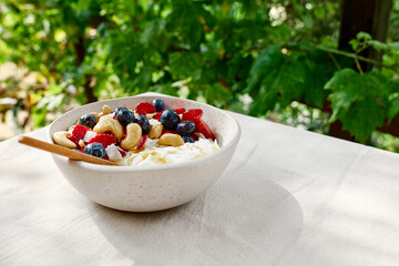 Coconut yogurt granola with strawberry, blueberry and cashew in white bowl. Concept of healthy breakfast, vegetarian meal, dieting, weight loss, healthy eating.