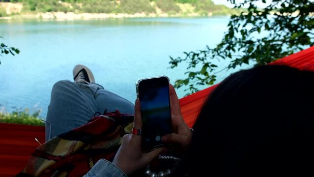 woman laying on hammock surfing social networks on the phone