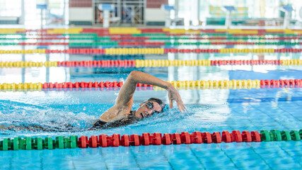 Sportswoman jumping off the diving block into the pool, sliding below the water, and swimming in...