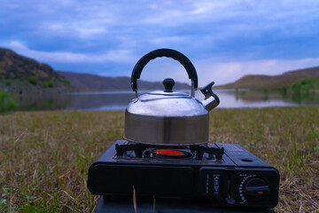 Close-up of a stainless steel kettle is heated on a camping gas stove against the background of a...