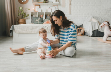 Beautiful young mother plays and teaches her baby 6 months old on the floor in the living room.mom...