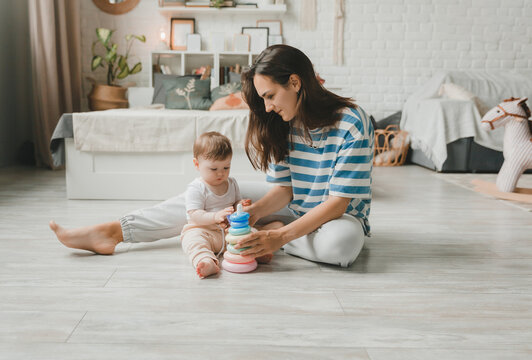 Beautiful young mother plays and teaches her baby 6 months old on the floor in the living room.mom and baby play with toys