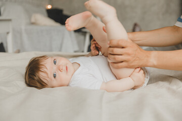 Mom makes a foot massage for a 6-month-old baby at home on the bed. mother plays with the baby at...