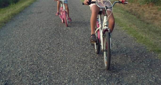 Slow Motion Close Up Shot of Two Bicycles Ridden by Little Girls on Countryside Road. Two Female Children Enjoying Their Summer Vacation Together on Family Retreat in Nature. Happy Childhood Memories