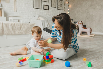 Beautiful young mother plays and teaches her baby 6 months old on the floor in the living room.mom and baby play with toys