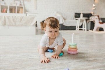 baby 6-9 months old playing with a colorful rainbow toy pyramid sitting in a white sunny bedroom. Toys for small children. Children's interior. A child with an educational toy.