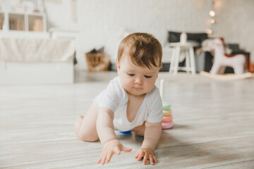 baby 6-9 months old playing with a colorful rainbow toy pyramid sitting in a white sunny bedroom. Toys for small children. Children's interior. A child with an educational toy.