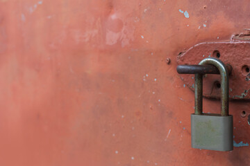 Background of old and rusty padlock was locked on scratching color surface of metal maroon door in abandoned ware house. Selective focus and copy space.