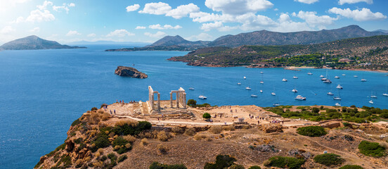 Panoramic view of the Temple of Poseidon at Cape Sounion at the edge of Attica, Greece, with moored sailboats in the bay during summer time