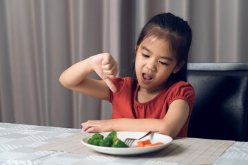 Little cute kid girl refusing to eat healthy vegetables. Children do not like to eat vegetables.