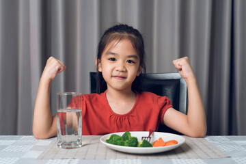 Kid shows strength of eats vegetables and nutritious food.