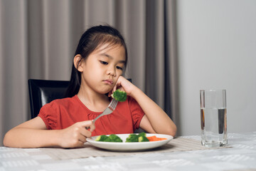 Little cute kid girl refusing to eat healthy vegetables. Children do not like to eat vegetables.