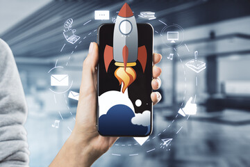 Female hand holding cellphone with creative rocket ship sketch on blurry office background. Content...