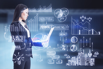 Attractive young european businesswoman using laptop with creative toned business sketch on blurry office interior background. Business strategy and finance concept.