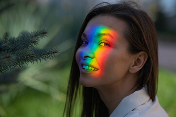 Portrait of caucasian woman with rainbow beam on her face outdoors.