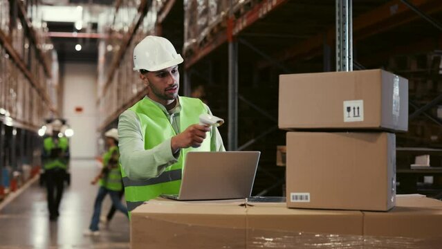 Positive Male Supervisor Scanning Parcels. Checking the Delivery Data Sitting in the Vast Logistic Centre and Busy Working People in the Background. Logistic Business Shipping and Delivery service.