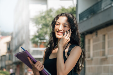 smiling student with folder and books and phone in the street