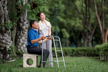 Asian daughter caring for father using leg support to walk, to accompany retired father to physical therapy, learning to walk with a happy smile
