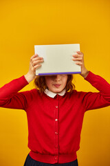 Portrait of happy teenage schoolgirl cover her face by book