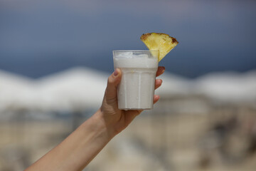 Woman hand with Pina colada cocktail with beach behind