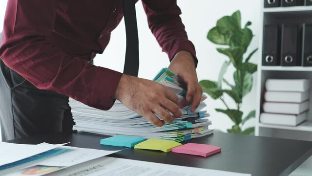 Businessman working in stacks of paperwork files for searching information unfinished documents about pile audit form on desk office and investigate financial doc in busy workload.