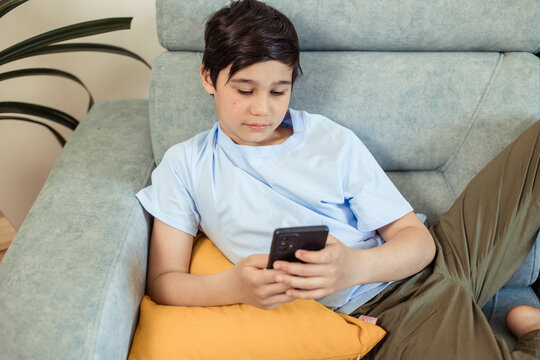 Portrait of a teenage boy on the couch in his room with a phone in his hands, looking at a smartphone, communication, online games, close up
