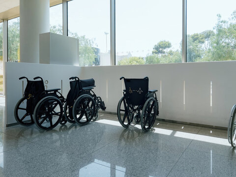 At airport, wheelchairs parked indoors by window, showcasing medical equipment and transportation facilities. No people present. Emphasis on accessibility and differing abilities.