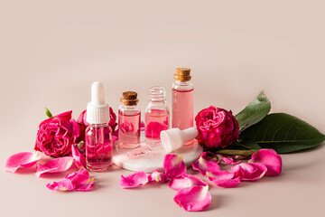 A set of cosmetics based on rose oil in various bottles among the buds of small roses on a beige background. home care