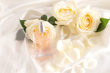 An elegant bottle of cosmetic product or spray leaned on a flower of a delicate tea rose. satin cream background. Blank layout for branding.