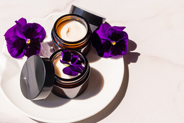 Obraz na płótnie Canvas Still life cosmetic. Natural cream for facial skin care in open cosmetic jars made of dark glass. rejuvenating effect. marble background. violets