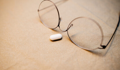 Fototapeta na wymiar A closeup of a fashionable eyeglass frame resting on a table, with its accompanying pill for vision care in the foreground.