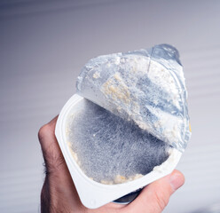 A lone hand controls a plastic recipient, holding moldy yogurt inside.