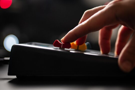 Daytime photo of fingers moving colorful faders on a music production studio desk.