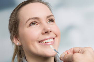 Close up of dentist using shade guide at woman's mouth to check veneer of teeth for bleaching
