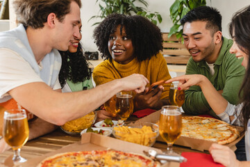 Group of multiethnic friends on a sofa eating pizza and drinking soft drinks at a home party, young...