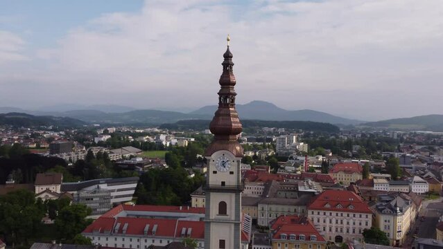 Aerial circling Klagenfurt Cathedral clock tower, revealing cityscape, Austria