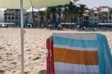Lonely beach chair under umbrella. Image without people of a beach lounger on the sand at the coast with a towel placed on top.