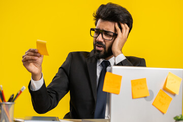 Tired exhausted indian businessman working on laptop at office with many sticker task inscriptions....