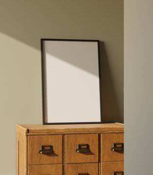 black wooden frame mockup standing on the wooden drawer leaning on the green wall lit by sunlight