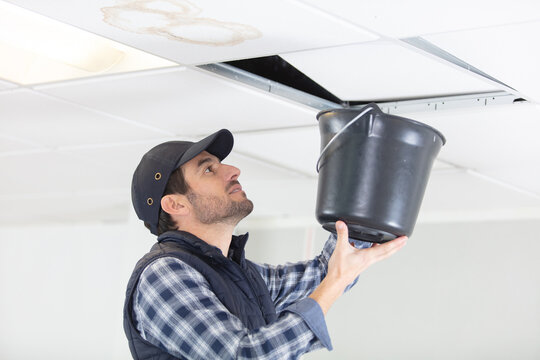 handyman holds bucket under ceiling panel