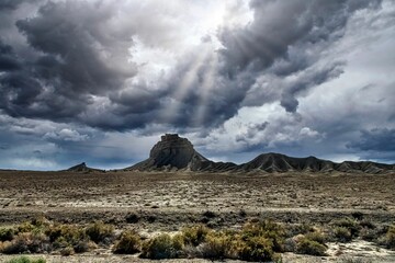 Obraz na płótnie Canvas Shiprock view with gloomy and cloudy sky with sun rays shining through and brightening around
