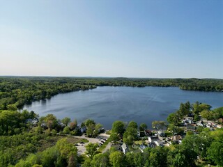 Drone view of Lake Attitash surrounded by greenery on a sunny day in Massachusetts