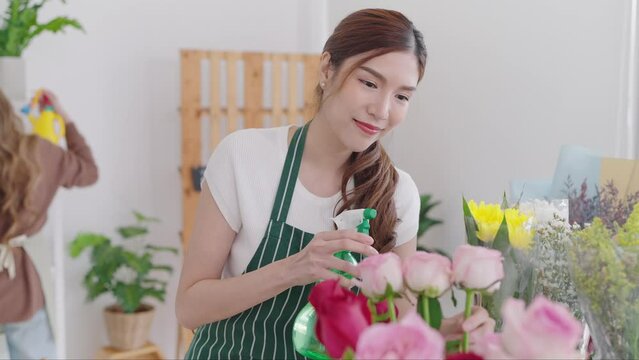 Beautiful asian woman florist spray water on flowers in flower shop add moisture and vitality to the flowers and to prevent flower from wilting in a flower shop. Florist concept, Small business owner