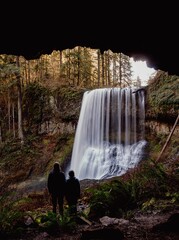 People admiring a picturesque waterfall cascading out of a natural cave in a tranquil setting.