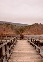 Young man and woman walk across a picturesque wooden bridge over a tranquil lake.