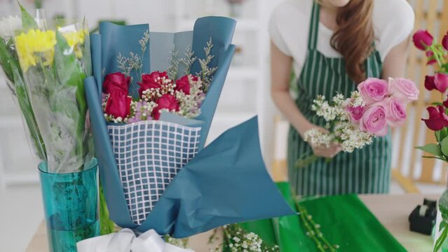 Woman florist in apron working in flower shop. Woman florist creating beautiful rose flowers bouquet for selling and delivery order to the clients. Florist concept